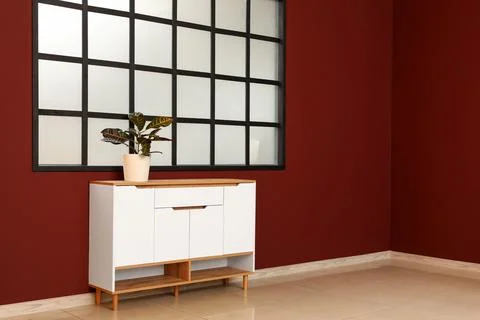 Interior of big empty room with window and houseplant on commode near burgund Stock Photos