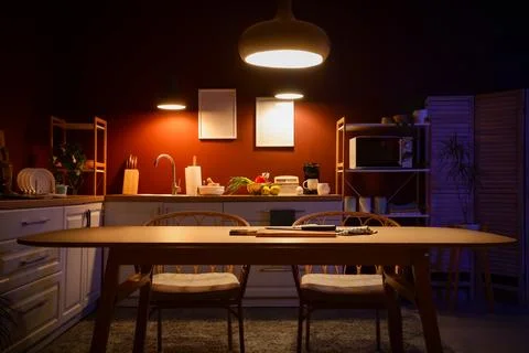 Interior of dark kitchen with counters, dining table and glowing lamps Stock Photos