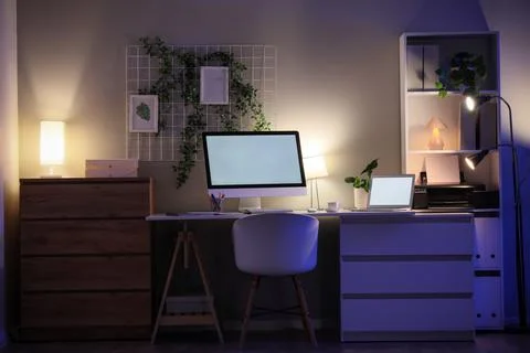 Interior of dark office with workplace, pin board, plants and glowing lamps a Stock Photos