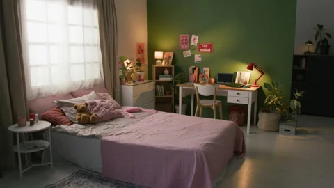 Interior of Dimly Lit Bedroom Featuring Cozy Bed, Bedside Table, Wooden Desk Stock Footage 335469880
