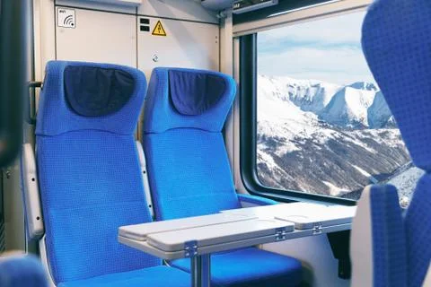 Interior of an empty passenger train with blue chairs and mountain views outside Stock Photos