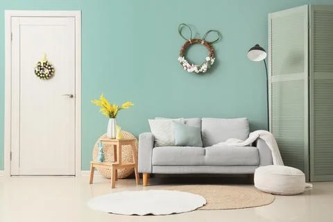 Interior of festive room with sofa, folding screen, stepladder and Easter wre Stock Photos