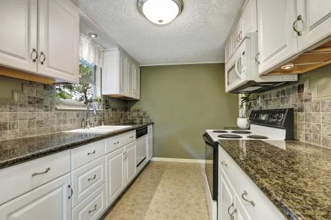 Interior of kitchen room with white cabinets, granite tops, natural stone bac Stock Photos