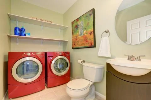 Interior of laundry room with modern red appliances, toilet and vanity cabinet.  Stock Photos