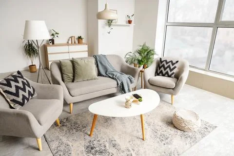 Interior of light living room with stylish mirror, grey sofa and armchairs Stock Photos