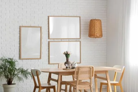 Interior of light room with blank frames, lamp and dining table Фото
