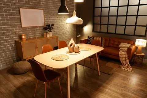 Interior of modern dining room with glowing lamps, sofa and table Stock Photos