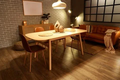 Interior of modern dining room with glowing lamps, sofa and table Stock Photos