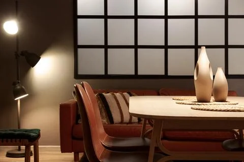 Interior of modern dining room with glowing lamp, sofa and table Stock Photos