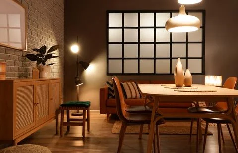 Interior of modern dining room with glowing lamps, table and sofa Stock Photos