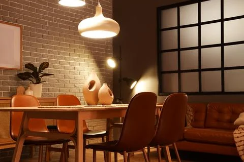 Interior of modern dining room with glowing lamps, sofa and table Stock Photos