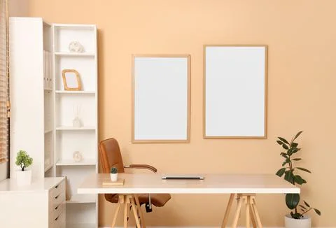 Interior of office with blank frames, workplace and shelf unit Фото