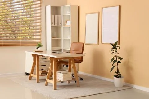 Interior of office with blank frames, workplace and shelf unit Фото