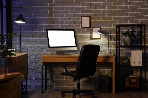 Interior of office with workplace, shelf unit and glowing lamps at night Stock Photos