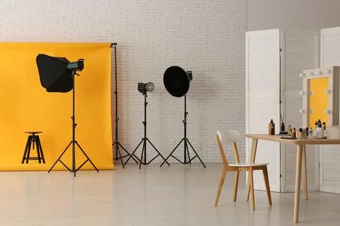 Interior of photo studio with yellow backdrop, makeup table and lighting equi Stock Photos
