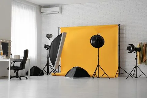 Interior of photo studio with yellow backdrop, makeup table and lighting equi Stock Photos