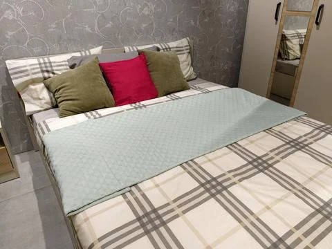 Interior of a room with a bed, pillows, one red, a wardrobe, and a nightsta.. Foto stock