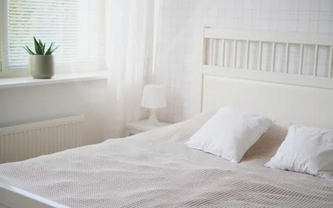 The interior of the room in white tones with a bed, bedside table, table lamp Stock Photos