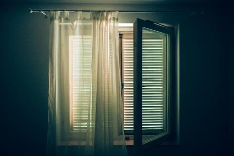 Interior shot from a dim room looking toward an open window with white curt.. Stock Photos