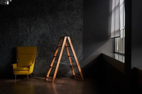 Interior with stepladder and a large yellow armchair on a black wall. Sun and Stock-Fotos