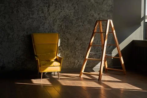 Interior with stepladder and a large yellow armchair on a black wall. Sun and Stock Photos