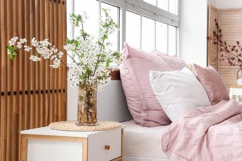 Interior of stylish bedroom with bed, bedside table and vase of blooming tree Stock Photos