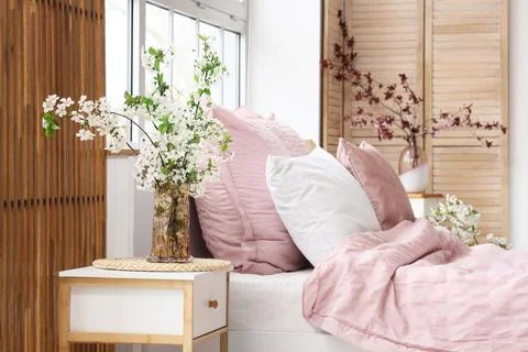 Interior of stylish bedroom with bed, bedside table and vase of blooming tree Stock Photos