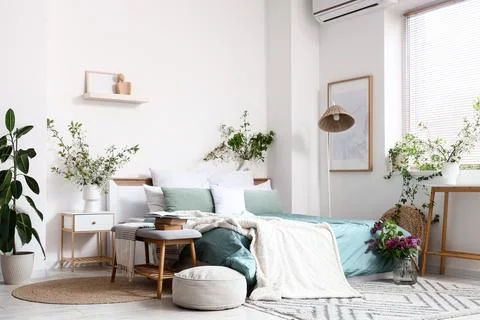 Interior of stylish bedroom with bench, bedside table, pouf and blossom branc Stock Photos