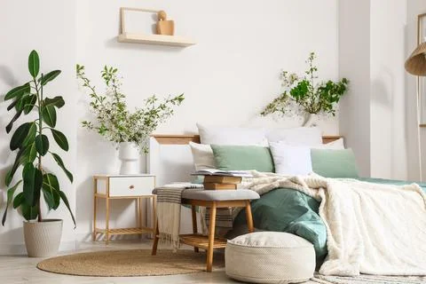 Interior of stylish bedroom with bench, bedside table, pouf and blossom branc Stock Photos