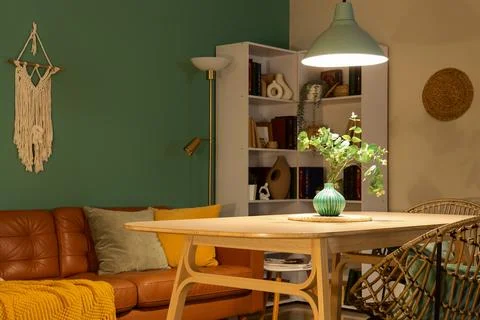 Interior of stylish dining room with brown sofa, table and glowing lamp at ev Stock Photos