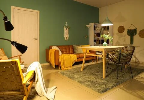 Interior of stylish dining room with brown sofa, table and glowing lamp at ev Stock Photos