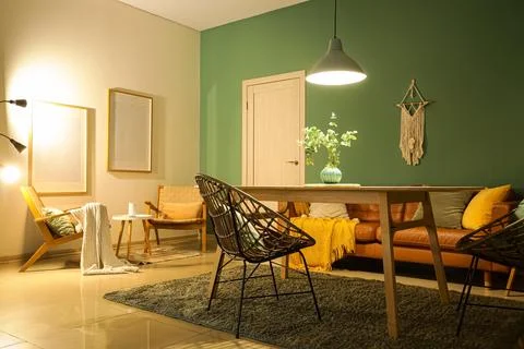 Interior of stylish dining room with brown sofa, table and glowing lamp at ev Stock Photos