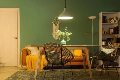 Interior of stylish dining room with brown sofa, table and glowing lamp at ev Stock Photos