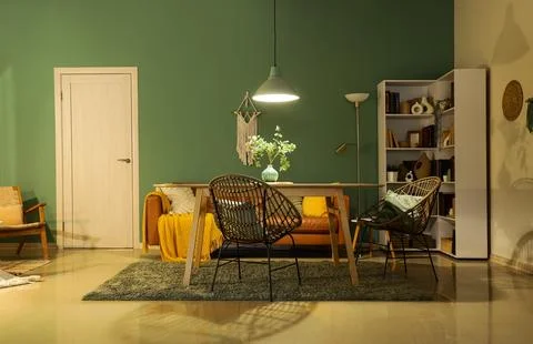 Interior of stylish dining room with brown sofa, table and glowing lamp at ev Stock Photos