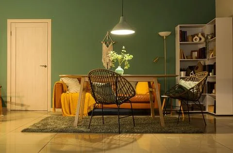 Interior of stylish dining room with brown sofa, table and glowing lamp at ev Stock Photos