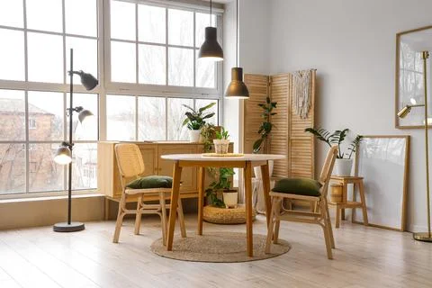 Interior of stylish dining room with table, houseplants, big window and glowi Stock Photos