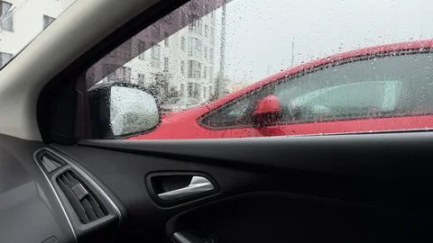Interior view from inside a car looking out a rain-covered window at a parked Stock Photos