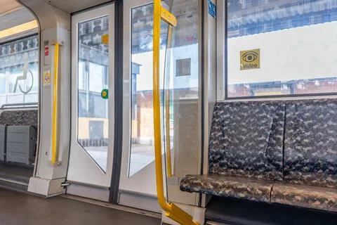 Interior view of a modern train with patterned seats and yellow poles. Stock Photos
