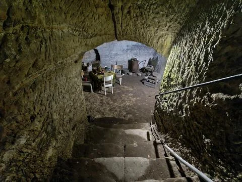 Interior view mossy stone cave dining area with worn wooden chairs metal st.. Stock Photos