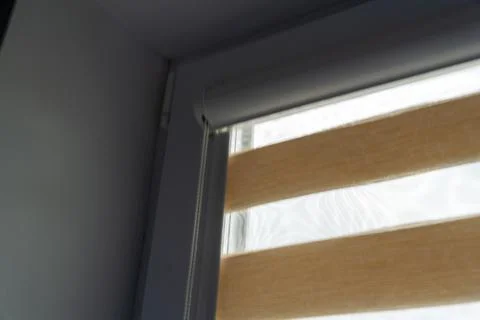 Interior view of a partially opened window with beige roller blinds filtering Stock Photos