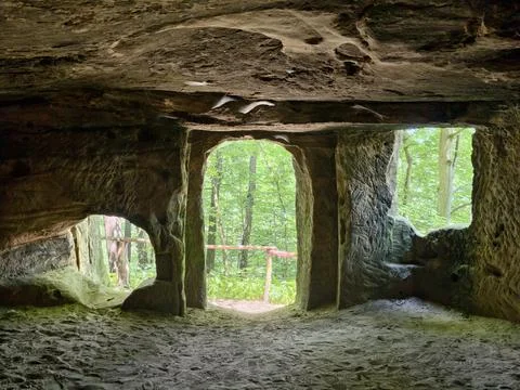 Interior view of sandstone cave opening toward leafy forest, with carved co.. Photos