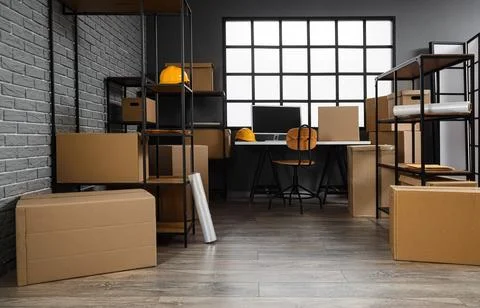 Interior of warehouse with workplace, shelf units and cardboard boxes Stock Photos
