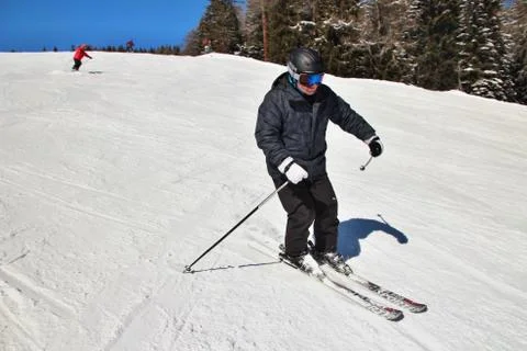 Intermediate man skiing in Alps on ski slope, side perspective, forest in b.. Stock Photos