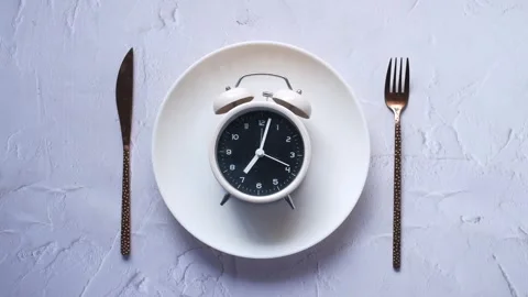 Intermittent fasting concept with alarm clock on white plate with gold knif.. Stock Footage 332472982