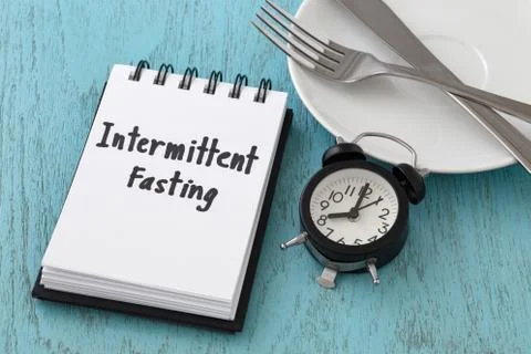 Intermittent fasting word on notepad with clock, fork and knife on white plat Stock Photos