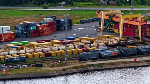 Intermodal terminal with containers, trains, and cranes near water in drone Stock Footage 313905700