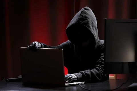 International hacker in black pullover and black mask trying to hack government Stock Photos