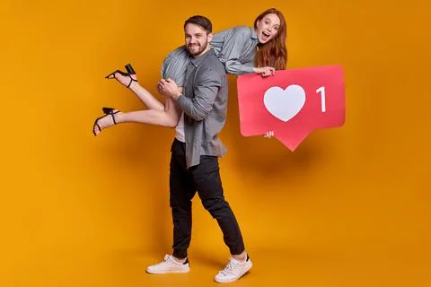 Internet blogging. Portrait of joyful couple in party wear holding heart like Stock Photos