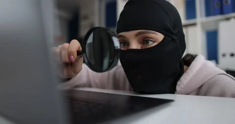 Internet theft and persons in balaclava with magnifying glass behind laptop Stock Footage 198003438