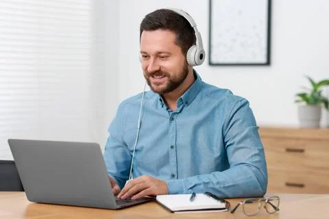 Interpreter in headphones having video chat via laptop at wooden table indoor Stock Photos